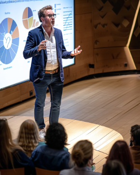 Conferencista empresarial presentando gráficos de análisis y datos financieros en una charla para un grupo de profesionales. La presentación visual apoya la explicación de estrategias de negocio y crecimiento. La imagen refleja la experiencia de más de 20 años en consultoría empresarial