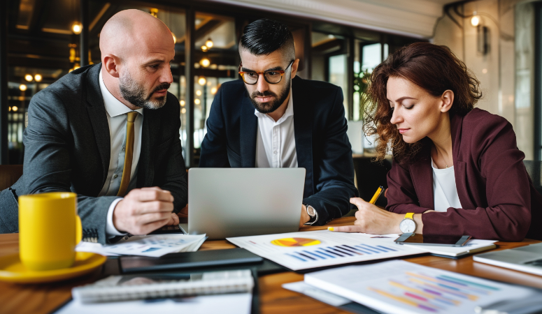 Grupo de consultores empresariales trabajando en equipo en una reunión, revisando datos financieros y estrategias en un portátil. Los documentos con gráficos y análisis de desempeño están sobre la mesa, mostrando un enfoque colaborativo en la toma de decisiones para el crecimiento empresarial. La imagen representa el trabajo de consultoría y análisis de negocios